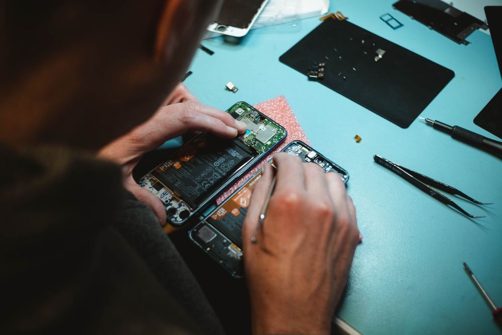 Man using tools to repair smartphone on blue/green table.