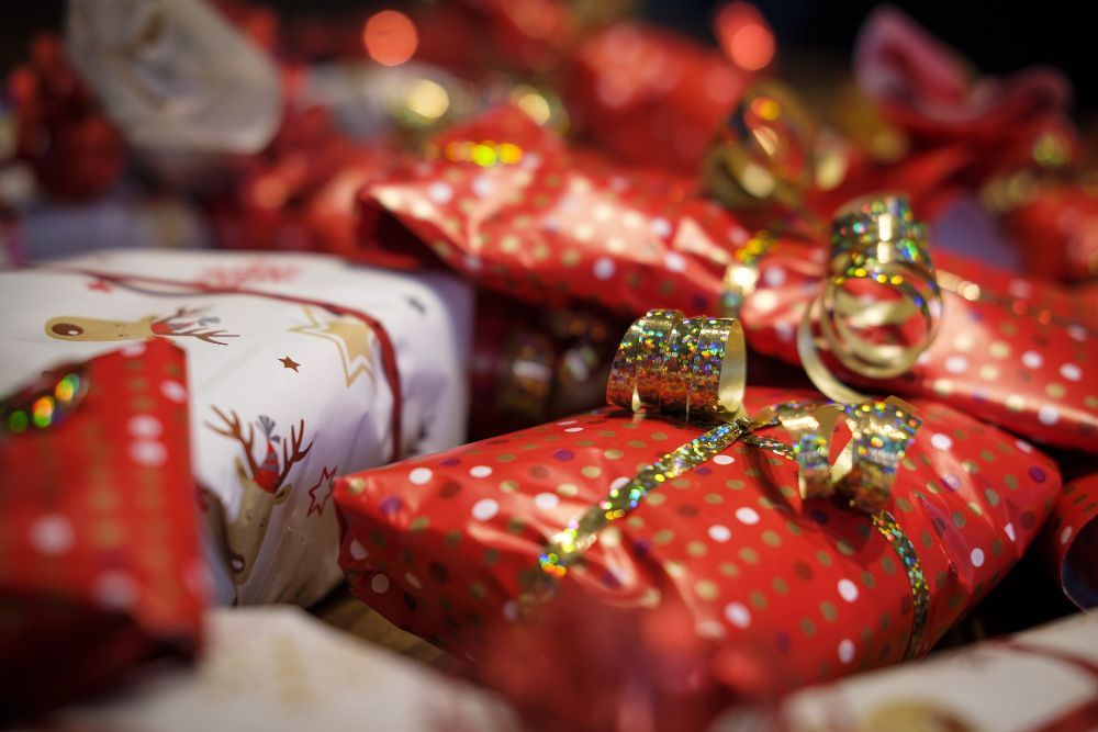 Pile of Christmas gifts wrapped in red and white wrapping paper, tied with sparkly gold bows.