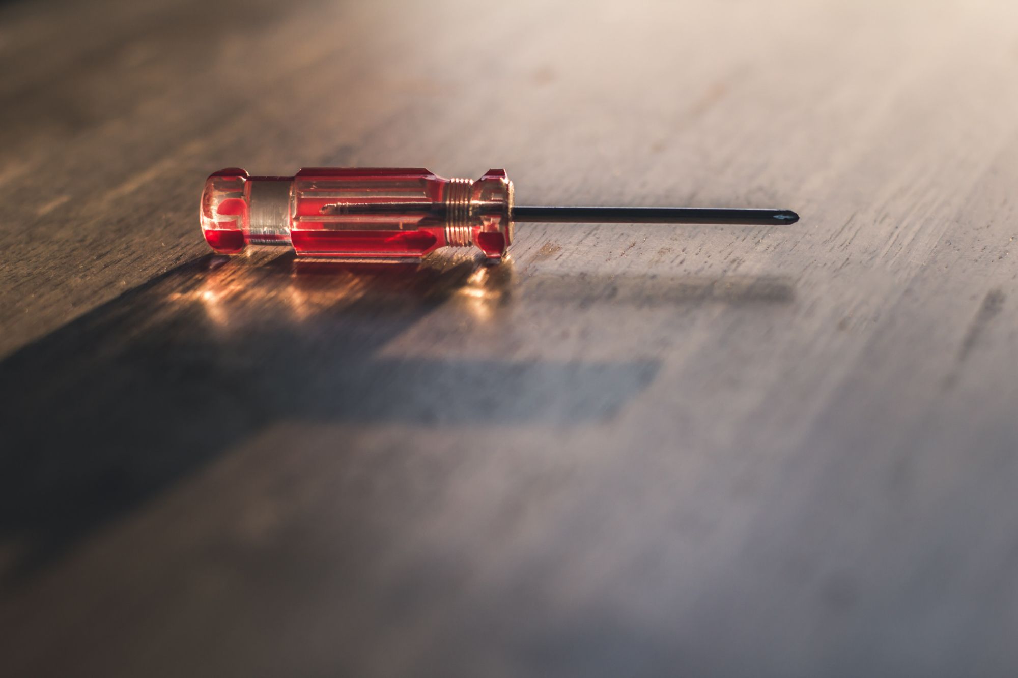 Red screwdriver on wooden floor with point facing to the right.