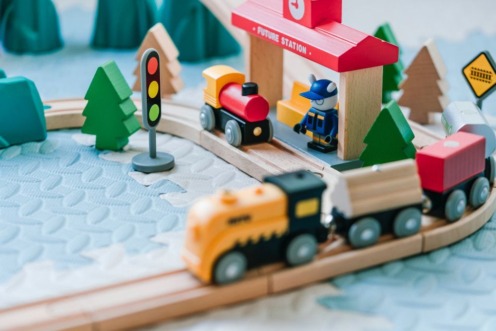 Colourful toy train set with train and train station in the foreground and toy trees in the background.