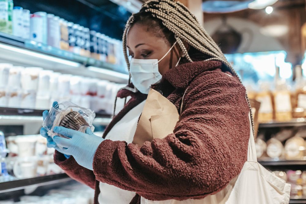 Lady in supermarket reading label on chocolate muffin packaging.