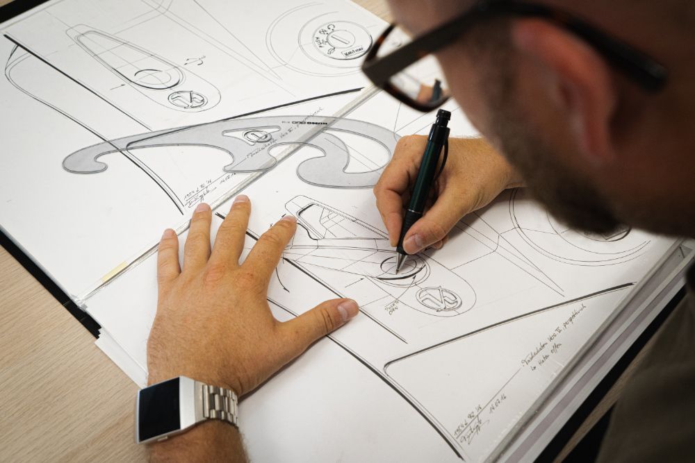 Man using pen to draw sketches of a scooter on an open notebook with white pages.