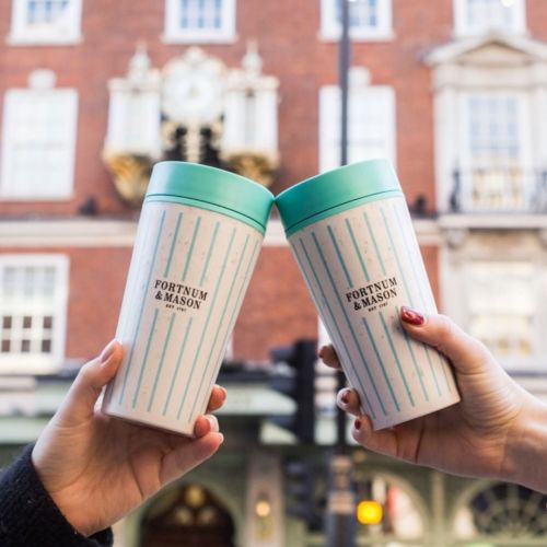 fortnum and mason branded coffee cups being held up outside their london store