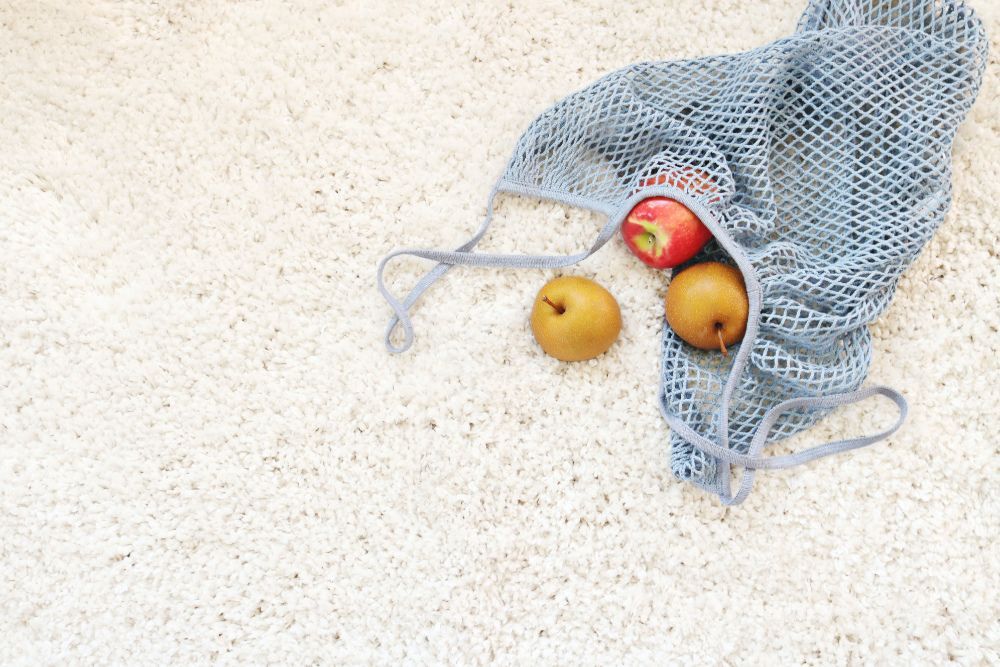 Grey tote bag containing apples on white carpet.