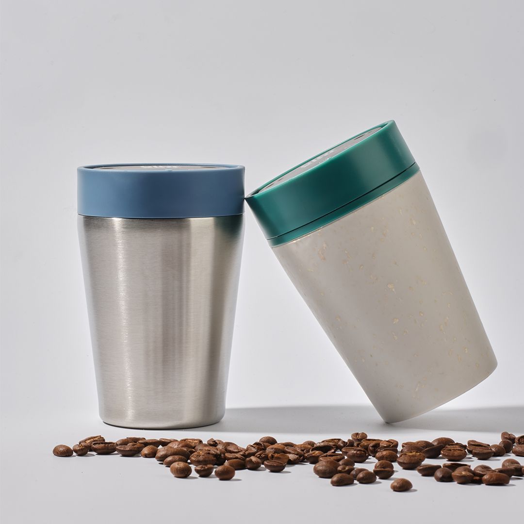 two coffee cups leaning on each other with coffee beans on the floor