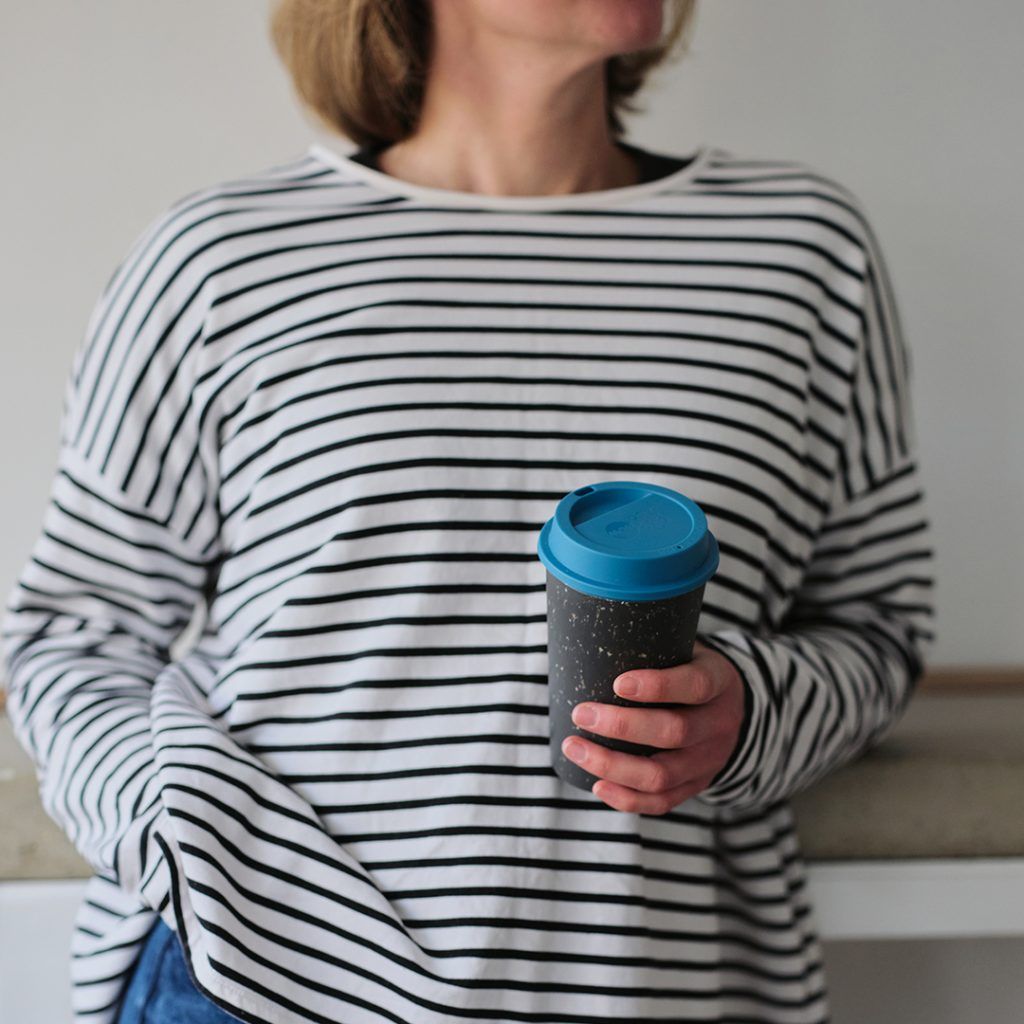 woman holding black reusable cup with blue lid