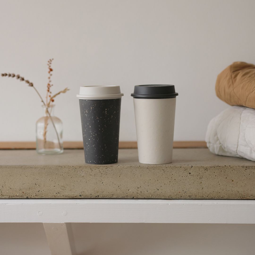 black reusable cup and white reusable cup on stone table
