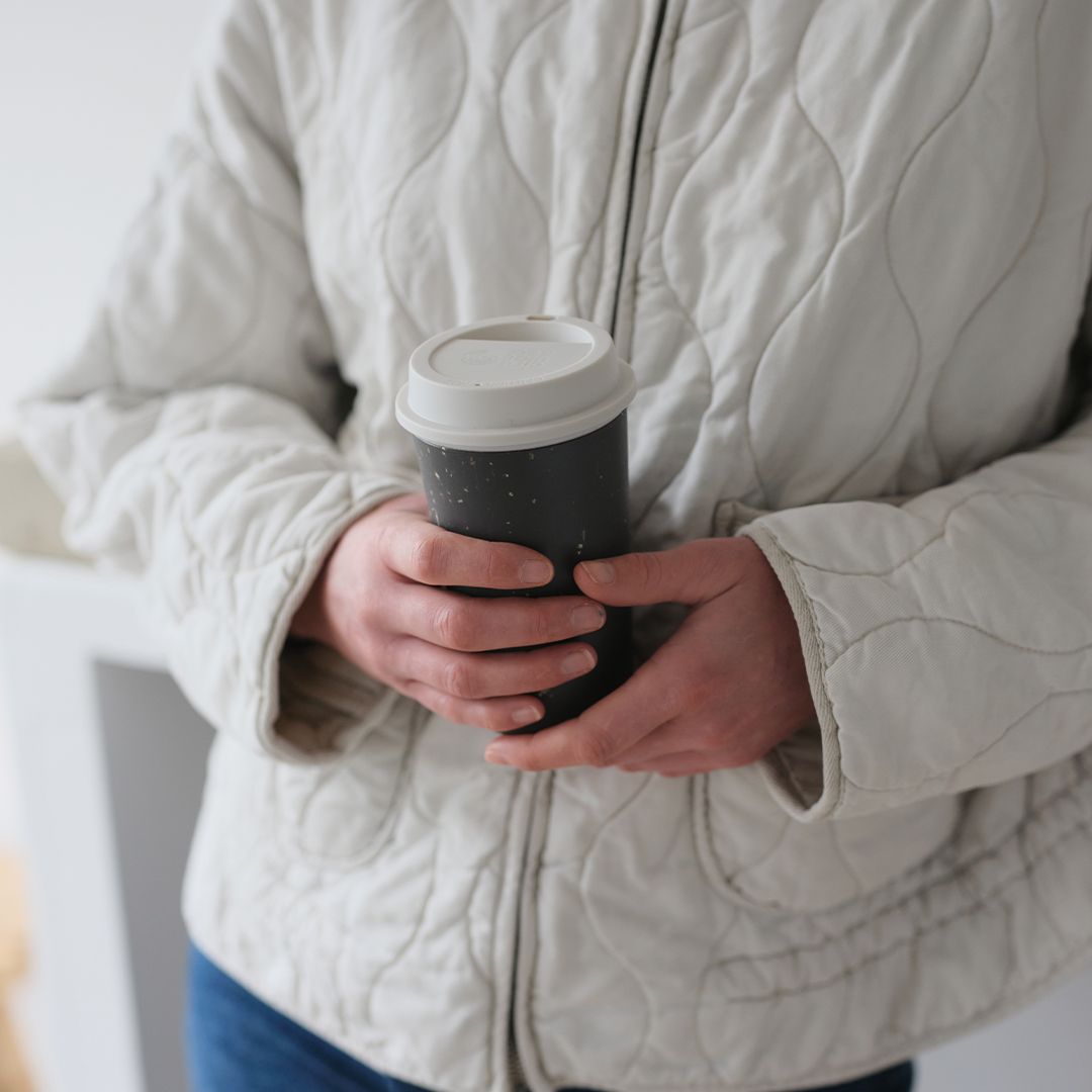 woman holding black reusable cup with white lid