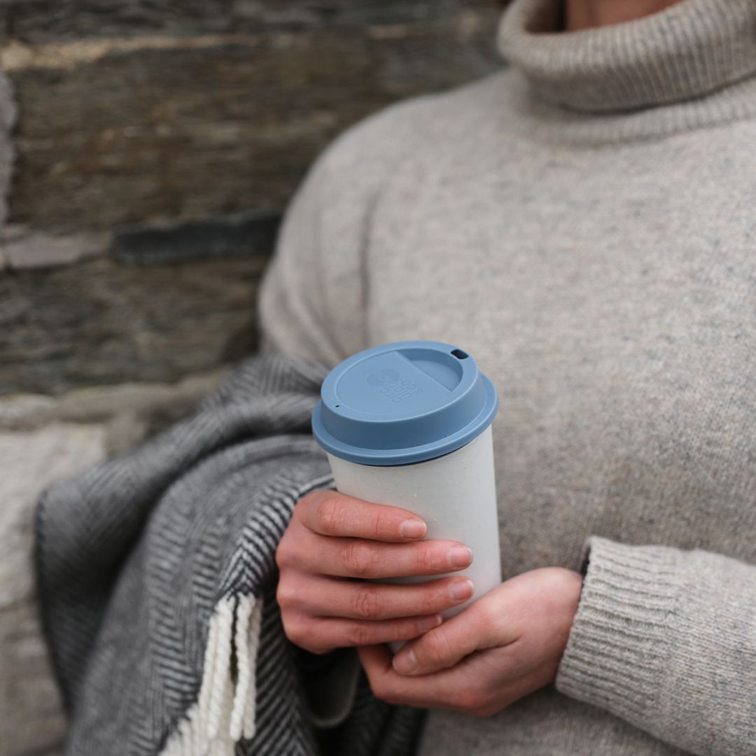 woman holding white reusable cup with blue lid