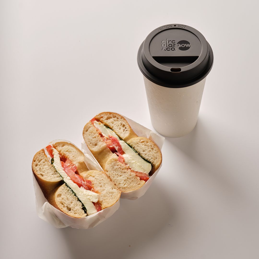 white reusable cup with black lid next to bagel