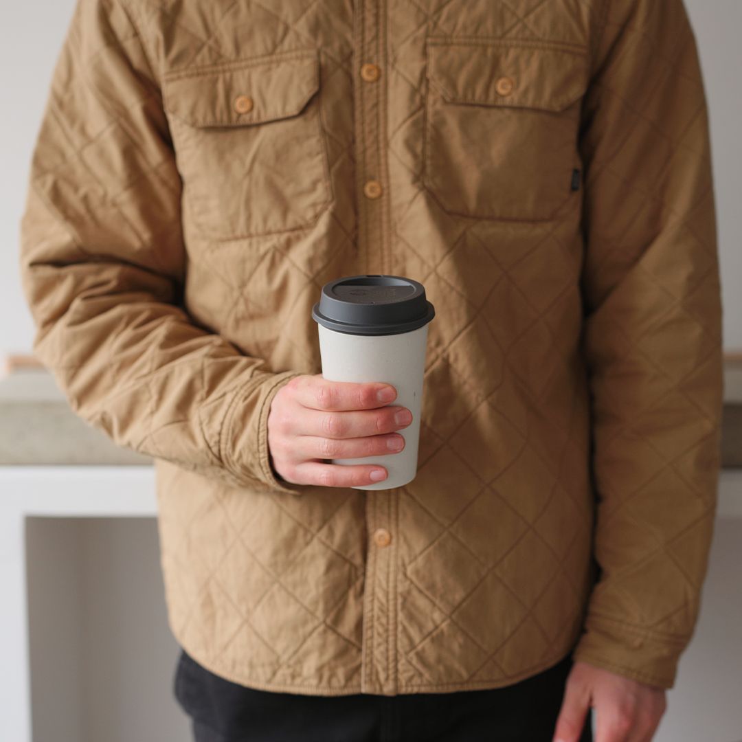 man holding white reusable cup with black lid