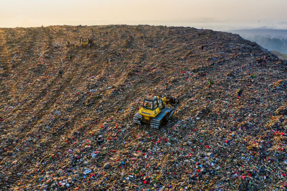 Yellow JCB digger driving up a large hill in a landfill.