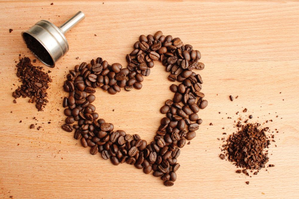 Coffee beans arranged in a love heart shape on a light brown table.