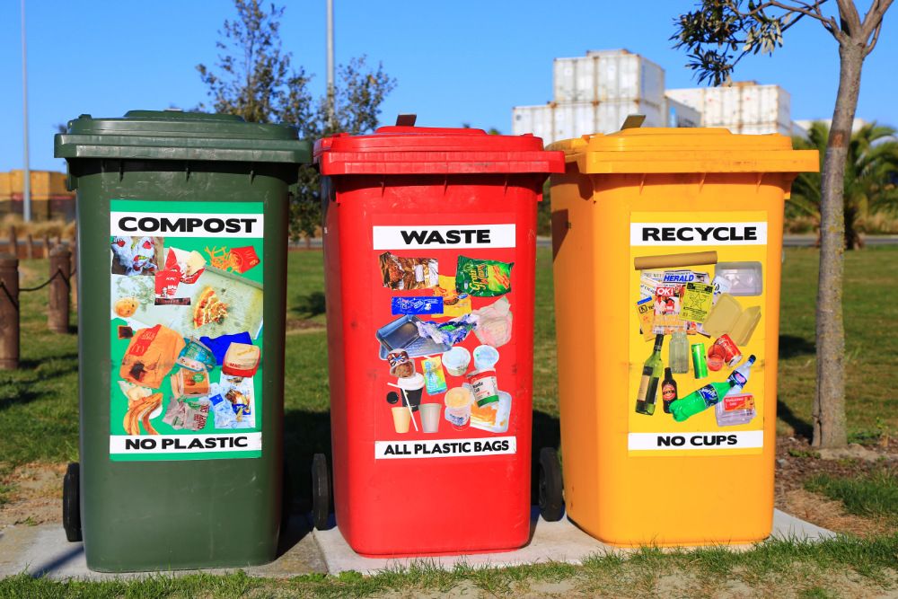 Green compost bin, red waste bin, and yellow recycling bin lined up side-by-side.