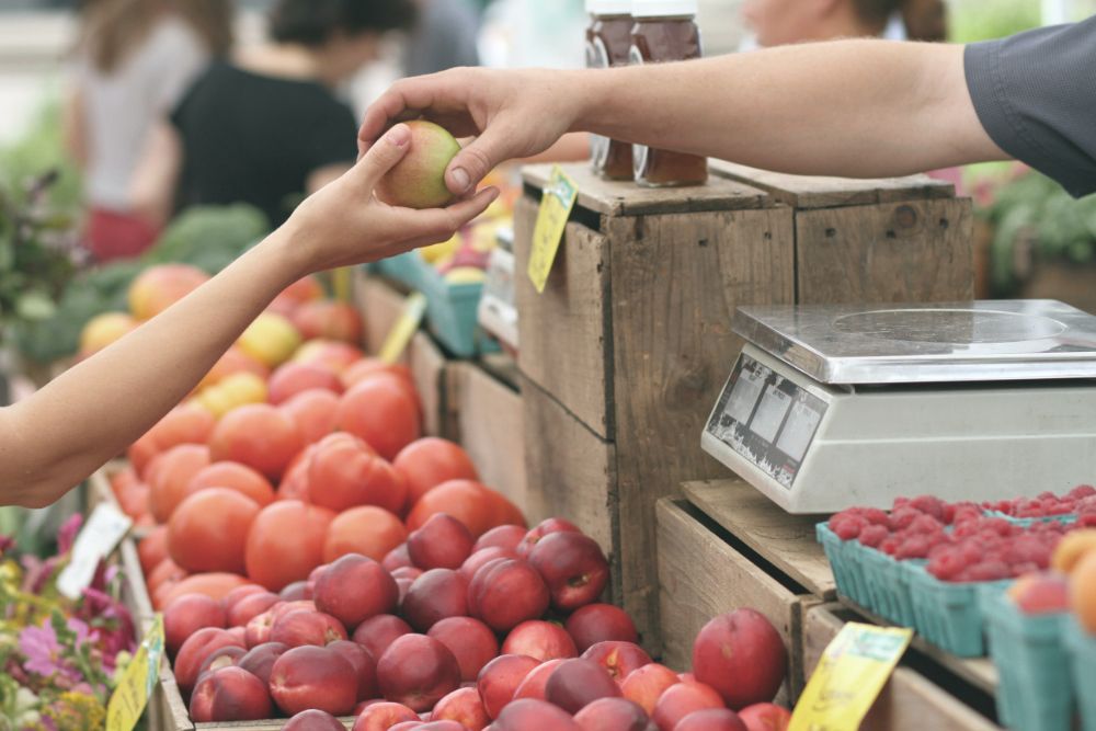 Cashier handing customer an apple at a farmer's market.