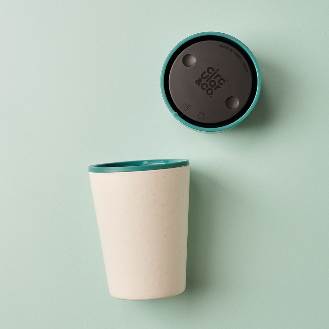 white reusable cup with green lid on green table