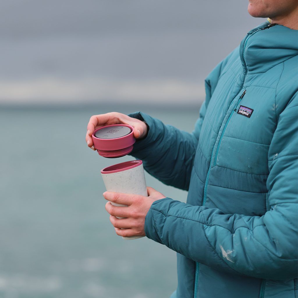 person in blue coat taking lid off of their reusable cup