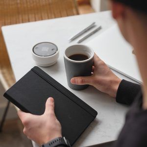 man holding black reusable cup and book