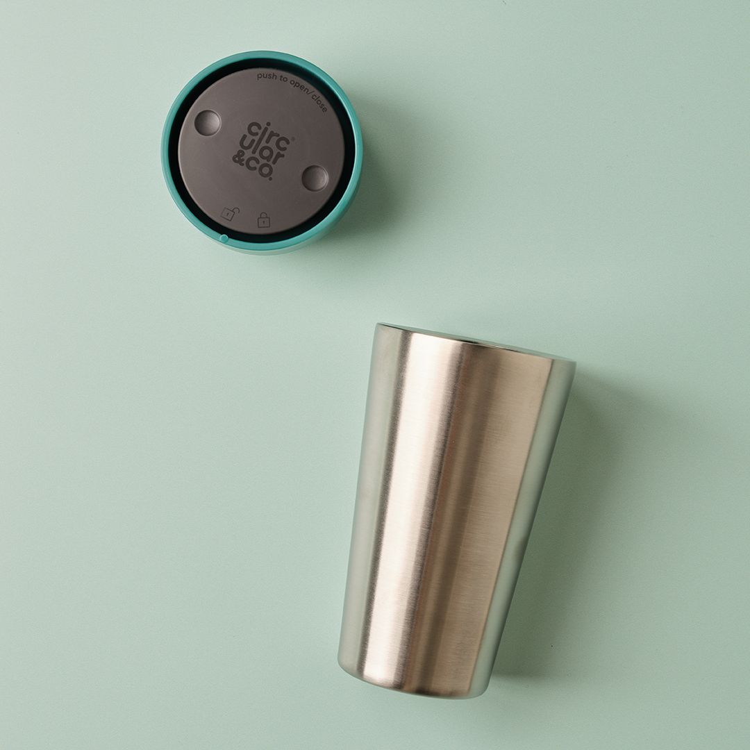 steel reusable cup with green lid on green surface