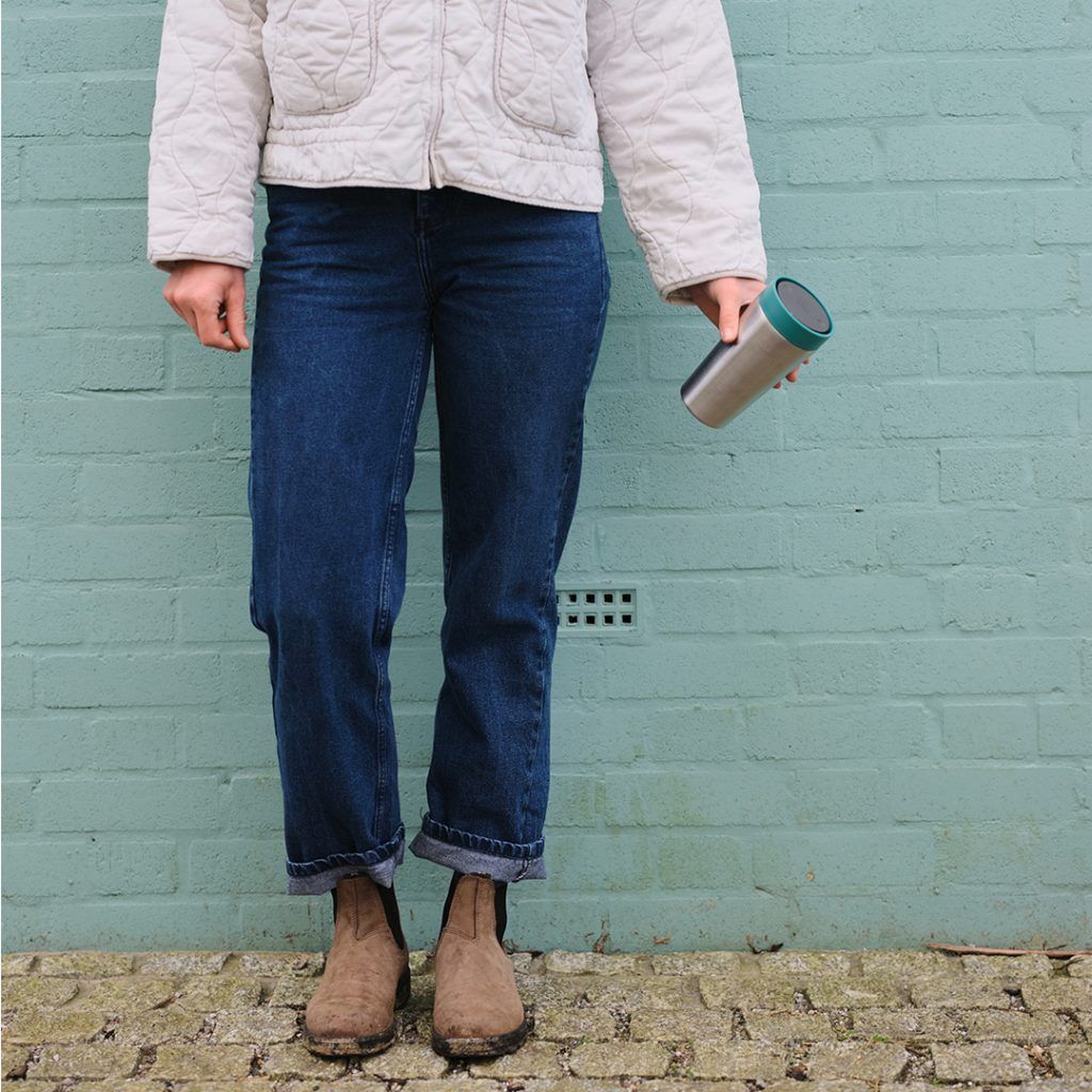 person holding steel cup with green llid in front of green brick wall