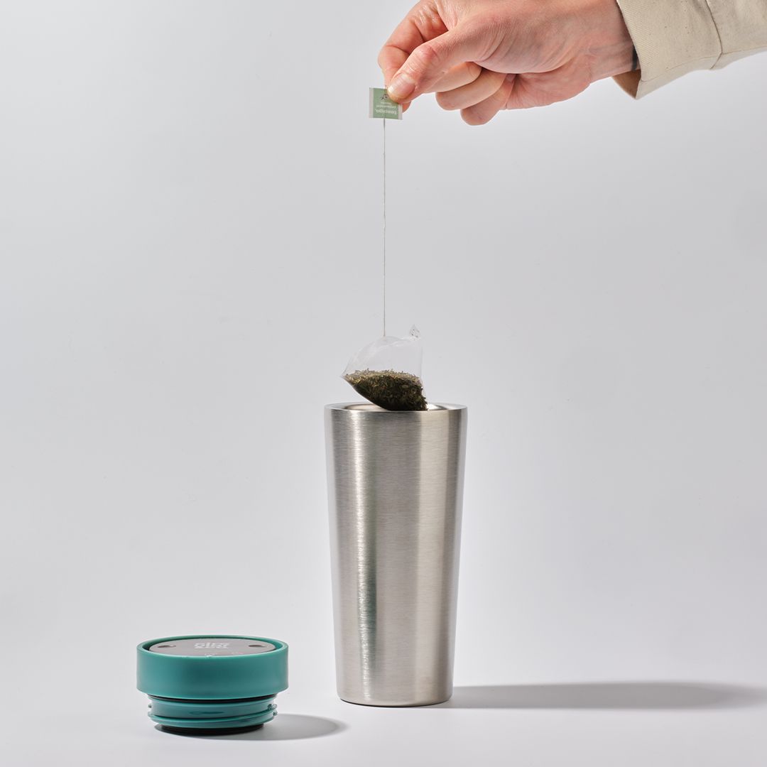 person dipping teabag into steel reusable cup