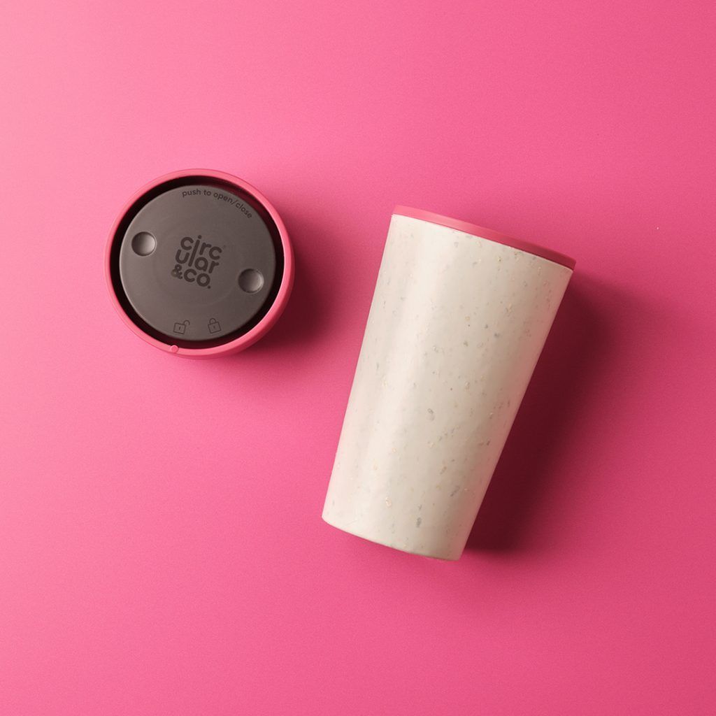 reusable cup laying down next to lid on pink table