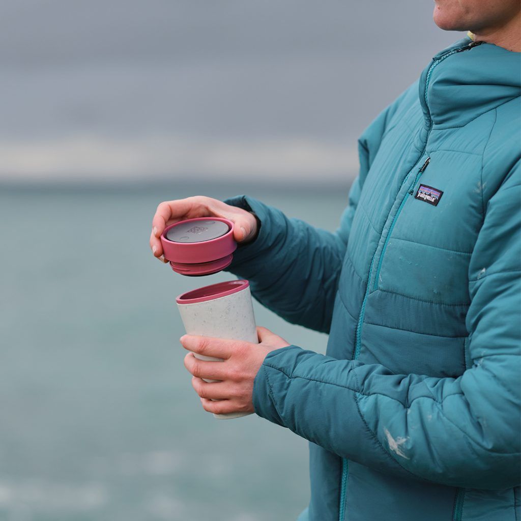 person holding reusable cup in front of the ocean