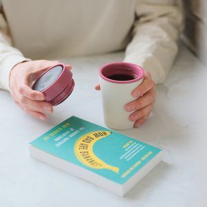 person holding white reusable cup with pink lid