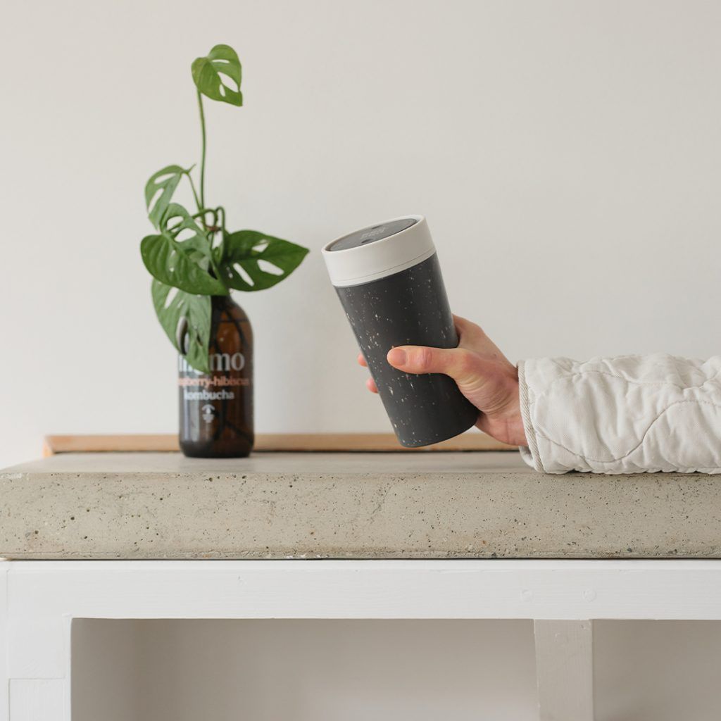 person holding black reusable cup with white lid on stone table