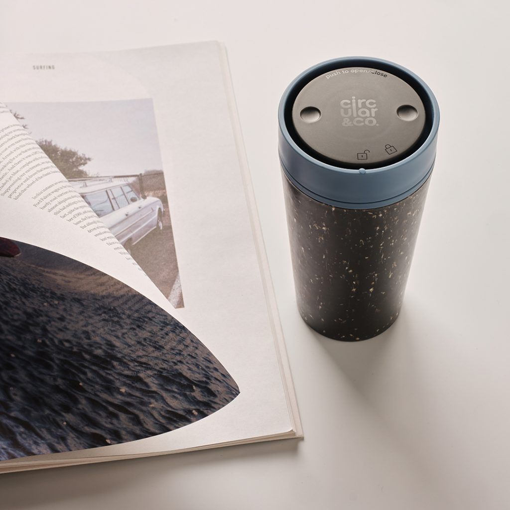 black reusable cup with blue lid next to magazine