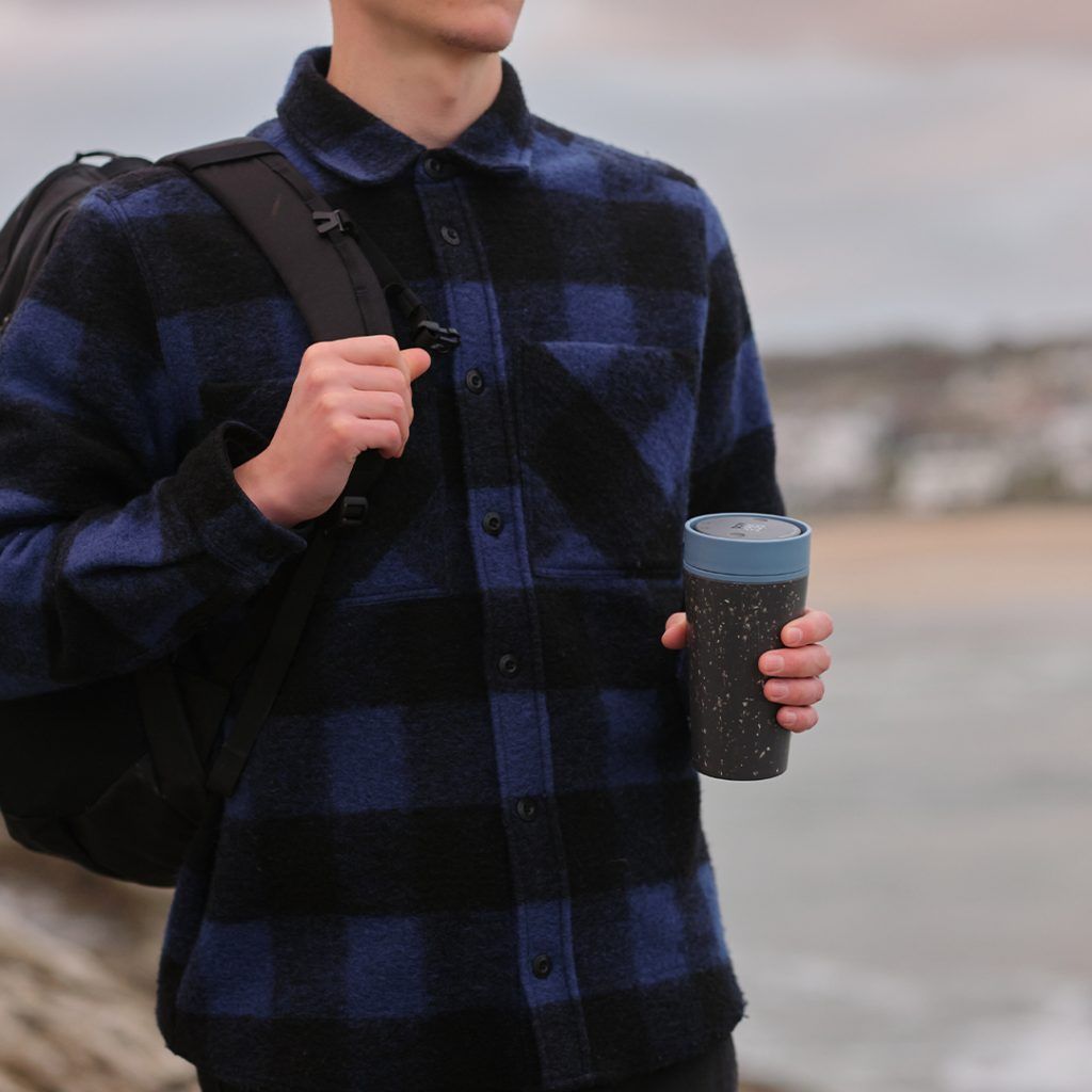 man in blue checkered shirt holding black reusable cup with blue lid