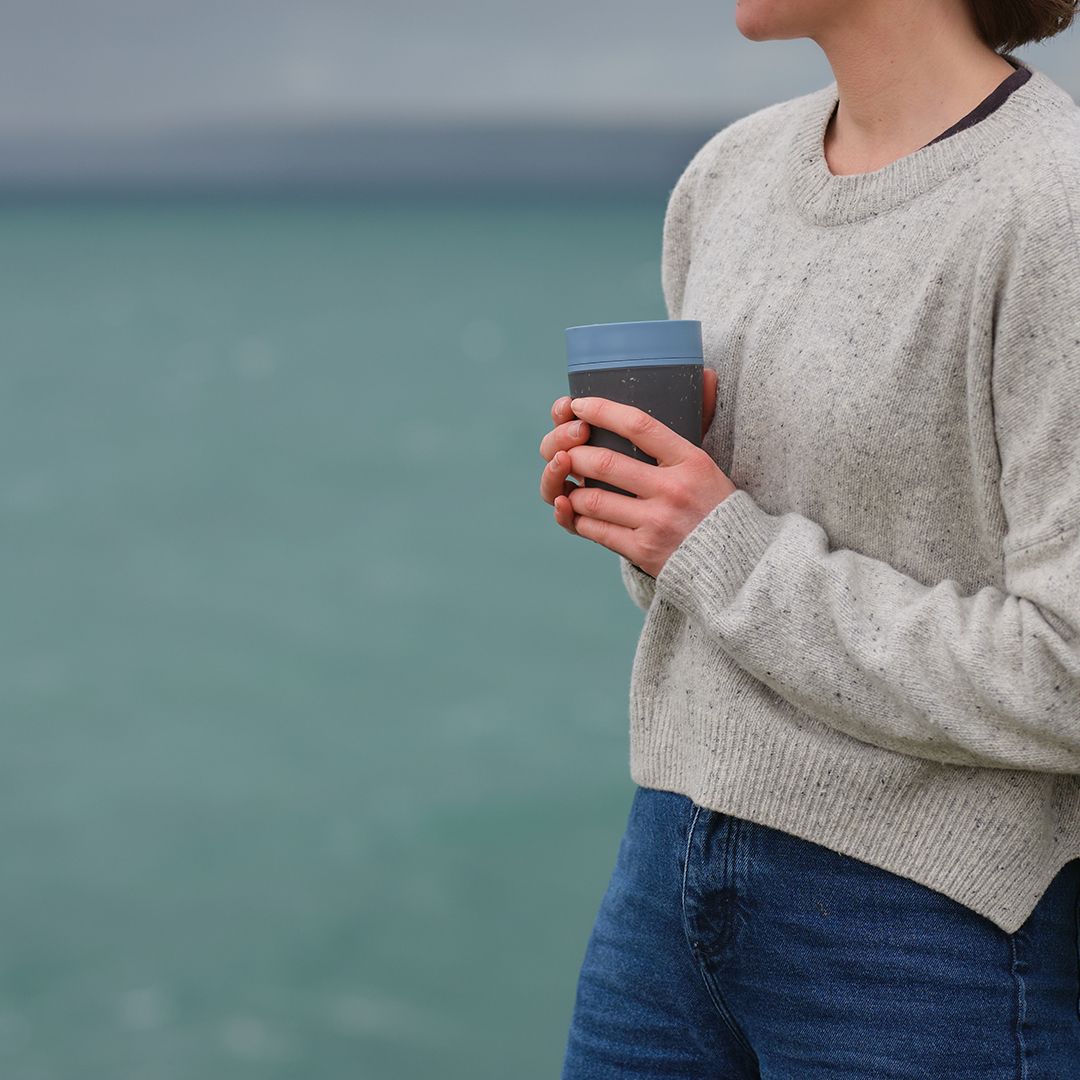 woman holding black reusable cup with blue lid