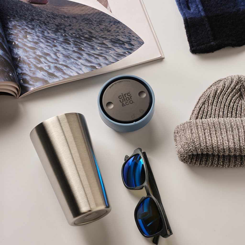 steel reusable cup with blue lid surrounded by accessories