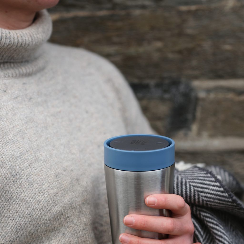 woman holding steel reusable cup with blue lid