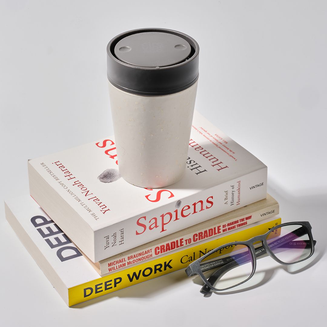 stack of books with white reusable cup and black lid on top of the books