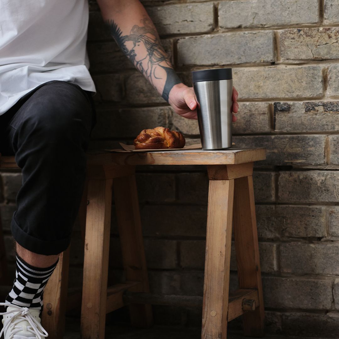 man sat on bench holding steel reusable cup with black lid