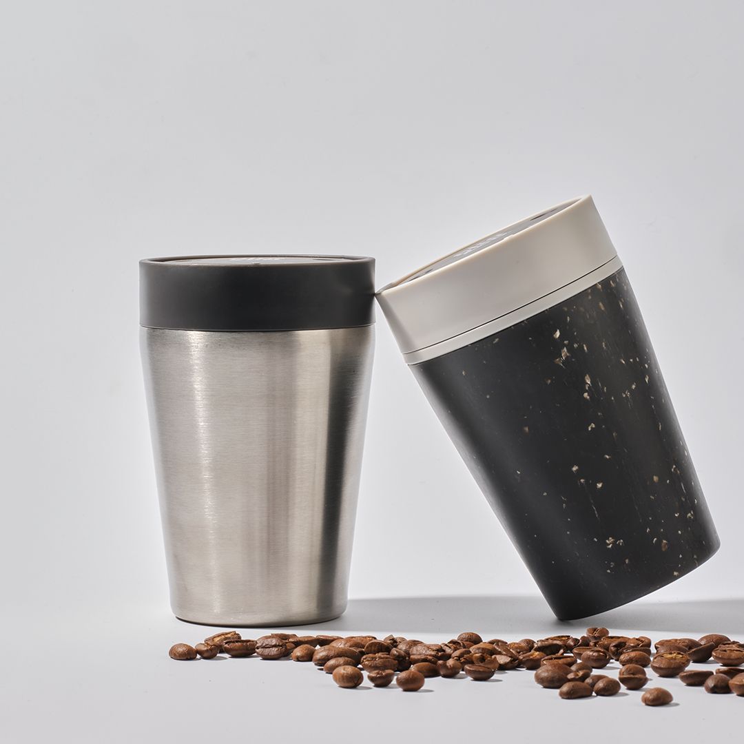 reusable cups leaning on each other with coffee beans in the foreground