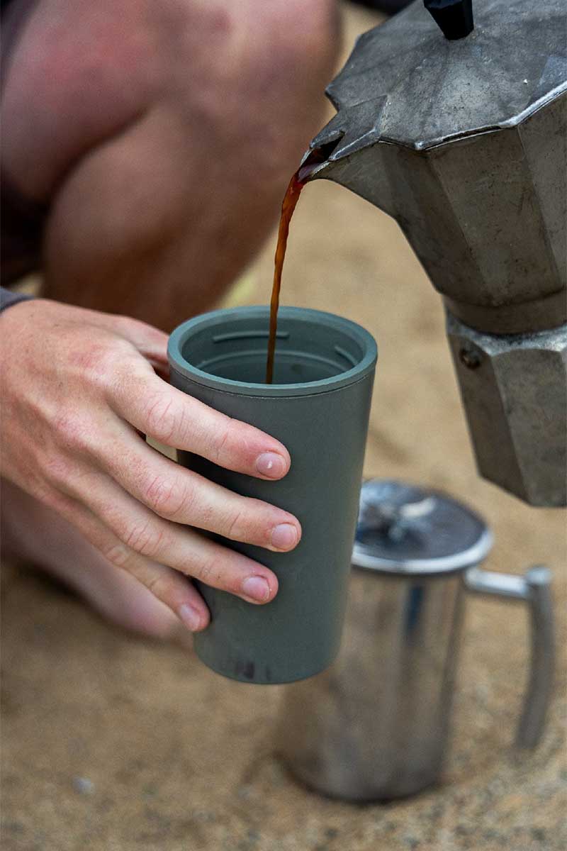 person dipping teabag into steel reusable cup